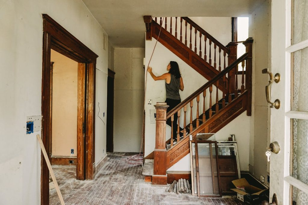 A woman working on home renovation featuring a wooden staircase.